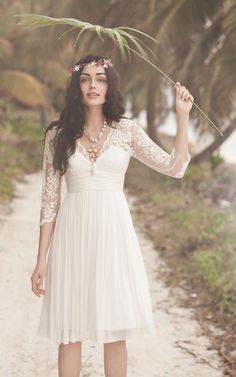 a woman in a white dress is holding a plant above her head and standing on a dirt path