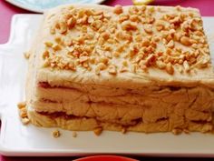 a square cake with nuts on top sitting on a plate next to a cup and saucer