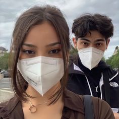 two people wearing face masks in front of the camera, one is looking at the camera