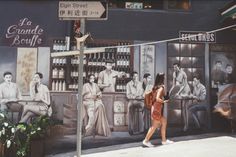 a woman walking down the street in front of a wall with pictures on it,