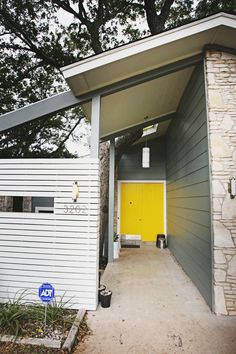 a yellow door is at the entrance to a white house with grey siding and stone pillars