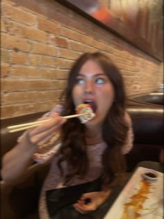 a woman sitting at a table with chopsticks in her mouth and eating food