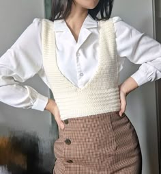 a woman wearing a white shirt and brown plaid skirt standing in front of a wall