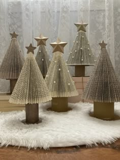 several small christmas trees made out of book pages on a white rug in front of a window