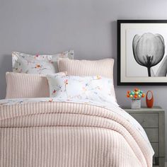 a bed with pink and white comforters in a bedroom next to a painting on the wall