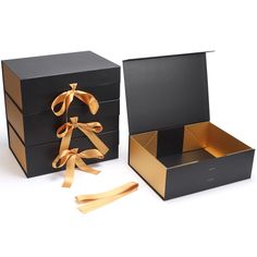 two black boxes with gold ribbon on the top and bottom, one opened to show an ornament