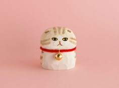 a white cat figurine with a red ribbon around it's neck on a pink background