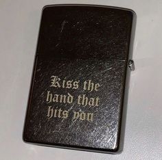 a black zippo with the words kiss the hand that hits pop written on it