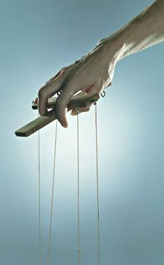 a hand holding a piece of wood with strings attached to it while another person holds something in the air