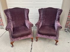 two purple velvet chairs sitting next to each other on the sidewalk in front of a garage door