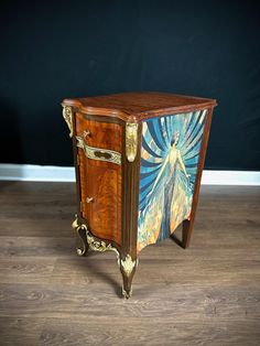 an ornate wooden cabinet with paintings painted on the doors and drawers, sitting on a hard wood floor