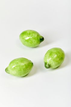 three green fruits sitting next to each other on a white surface with no one around them