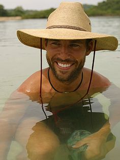 a man wearing a hat is in the water with his hands on his chest and smiling