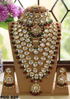 an elaborate necklace and matching earrings on display in front of a vase with purple flowers