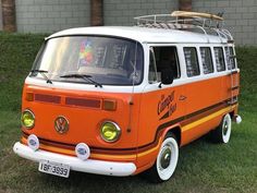 an orange and white vw bus parked on top of a grass covered field next to a building