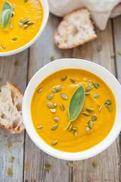 two white bowls filled with carrot soup and bread