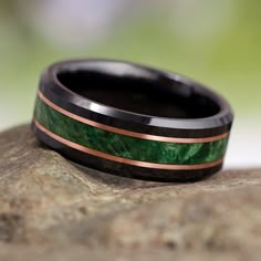 a black and green wedding band with copper inlays on top of a rock