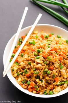 a bowl filled with rice and vegetables next to chopsticks on top of a table