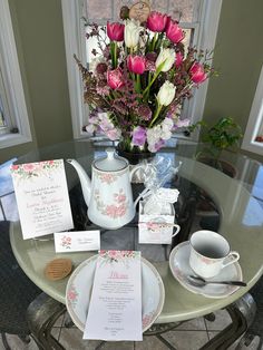 there is a table set with flowers and tea cups on top of the glass table