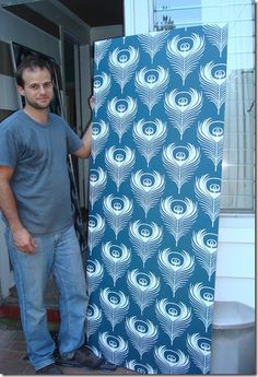 a man standing next to a blue and white wallpaper with an image of feathers on it