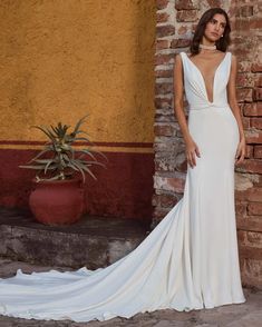 a woman standing in front of a brick wall wearing a wedding dress with an open back