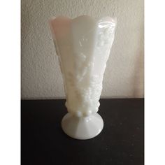 a white glass vase sitting on top of a black table with a wall in the background