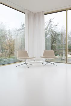 an empty room with two chairs in front of large windows that look out onto the trees outside