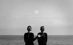 two women are sitting on the beach looking at the water