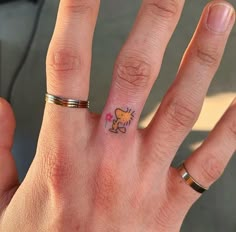 a person's hand with a small tattoo on the middle finger and an orange heart in the middle