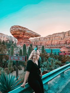 a woman standing on the side of a road next to a cactus and rock formation