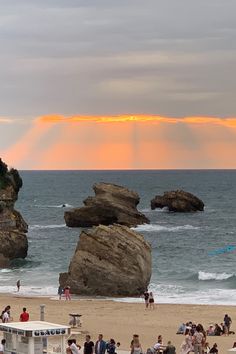 a group of people sitting on top of a sandy beach next to the ocean under a cloudy sky