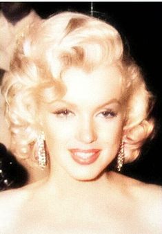 a woman with blonde hair wearing large earrings and a strapless dress is smiling at the camera