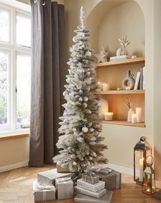 a white christmas tree with presents on the floor in front of it and a window