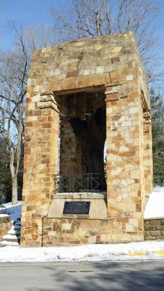 a stone structure with a clock on it in the middle of snow covered ground next to trees