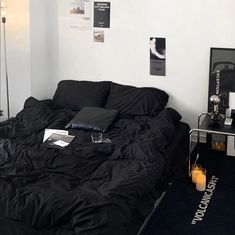 an unmade bed in a room with black sheets and pillows on the floor next to a table