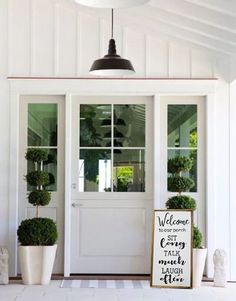 two potted plants on the outside of a white door with an advertisement above it