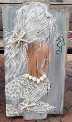 a wooden sign with a painting of a mermaid and starfish on it's side