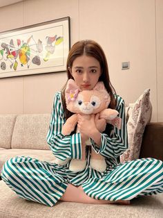 a woman sitting on a couch holding a teddy bear in her hands and wearing pajamas