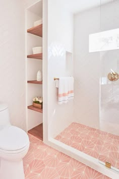 a bathroom with pink and white tiles on the floor, shower stall and shelves in the wall