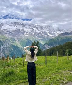 a woman standing on top of a lush green field next to a mountain covered in snow