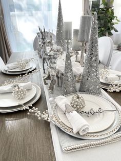 a dining room table set for christmas with silver and white decorations on the place settings