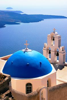 a blue domed building with two crosses on it's roof next to the ocean