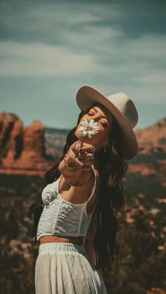 a woman with long hair wearing a white hat and holding a flower in her hand