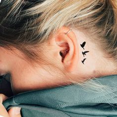 a woman with black birds on her left ear and behind her ear is a small bird tattoo