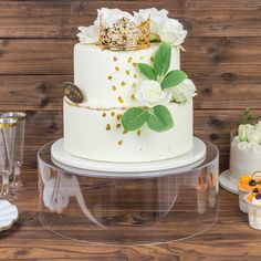 a wedding cake with white flowers and green leaves on the top is sitting on a table