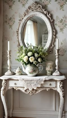 a white table topped with a vase filled with flowers next to a mirror and candles