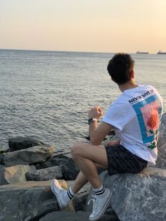 a man sitting on top of a rock next to the ocean