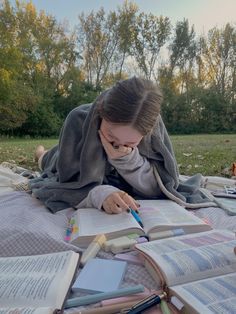 a woman laying on top of a blanket next to an open book while holding a pencil