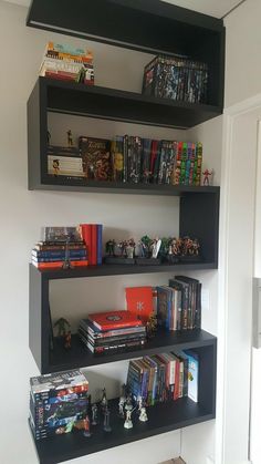 three black shelves filled with books and toys on top of each other in front of a white wall