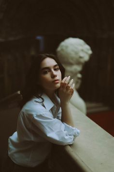 a woman leaning against a wall with her hands on her chin and looking off into the distance